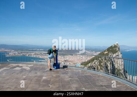 Woman at scenic view looking through public binoculars from Gibraltar upper rock. A woman exploring a high vantage point, using binoculars to take in Stock Photo