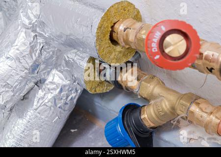 A close-up image of a heating pipe system with visible brass fittings, red and blue control valves, and foil-covered insulation material. Stock Photo