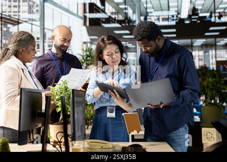 Diverse corporate staff gathered to brainstorm solutions together in the office, working to review reports for business growth. Workmates meeting and sharing insight on a successful strategy. Stock Photo