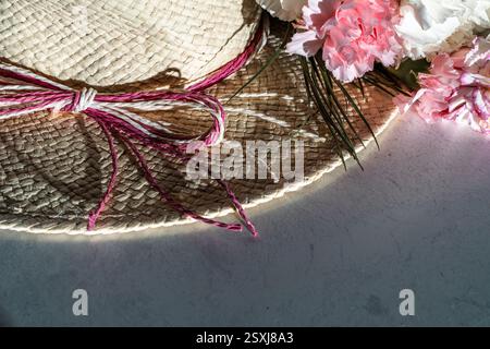 summer straw hat with twin ribbon and carnation flower heads in pink and white on marble table in hard sunlight, copy space, high angle view Stock Photo