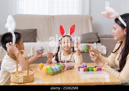 Easter fun time. A happy family sits at a table, decorating Easter eggs with paints, celebrating the holiday with creativity and joy. Stock Photo