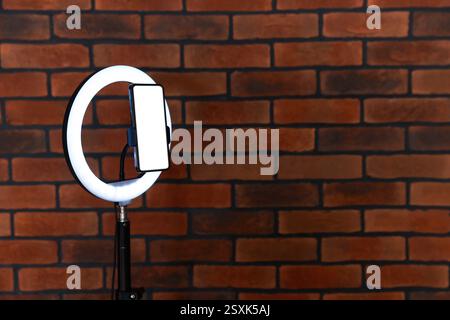 Ring lamp with smartphone against brick wall, space for text Stock Photo