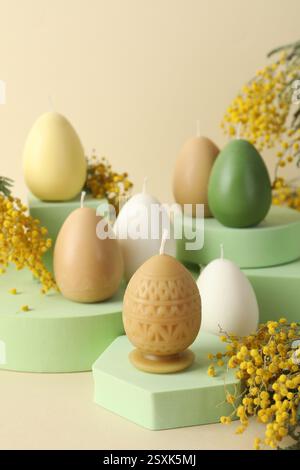 Beautiful egg shaped candles and mimosa flowers on beige background. Easter decor Stock Photo