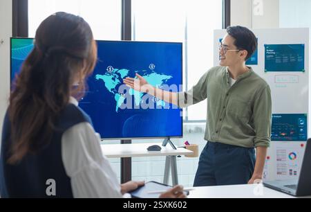 asian leader presenting a financial data and strategies in a modern office with charts and graphs displayed on a large screen Stock Photo