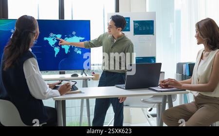 asian leader presenting a financial data and strategies in a modern office with charts and graphs displayed on a large screen Stock Photo