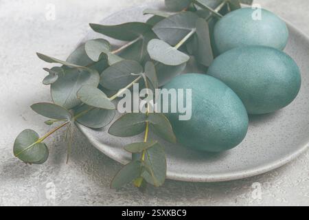 Easter colored eggs, in turquoise tones, on a gray plate, with a branch of eucalyptus, Easter card, top view, no people Stock Photo