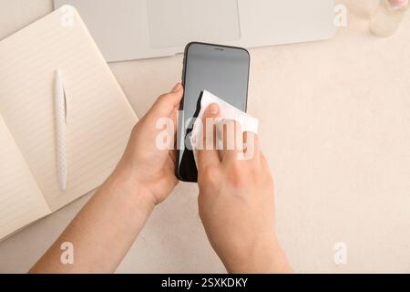 Young woman cleaning mobile phone on white table Stock Photo