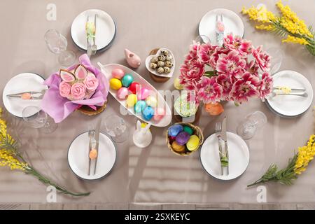 Festive stylish table setting with mimosa flowers, Easter cake and painted eggs Stock Photo