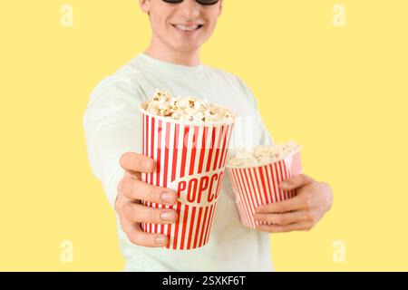 Young happy man in 3d eyeglasses with popcorn buckets on yellow background Stock Photo