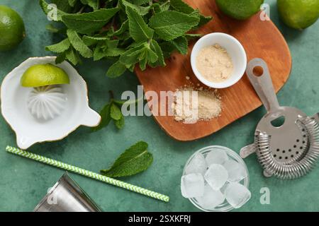 Wooden cutting board, juicer, strainer and ingredients for mojito on green background, closeup Stock Photo