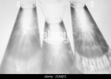 Fancy retro drinking glasses casting hard shadows on background. Grunge and noise effect applied, retro vintage style. Black and white image. Image co Stock Photo