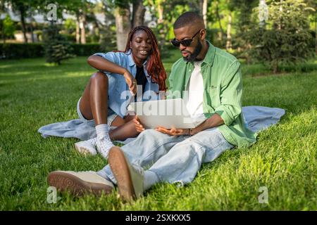 Calm African American couple sits under trees, studying online. Man browses exam resources on gadget Stock Photo