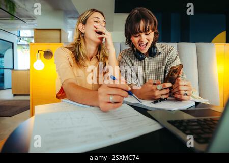 Two friends relax while studying, using social media for a break in a contemporary setting. Their laughter and connection highlight friendship and enj Stock Photo