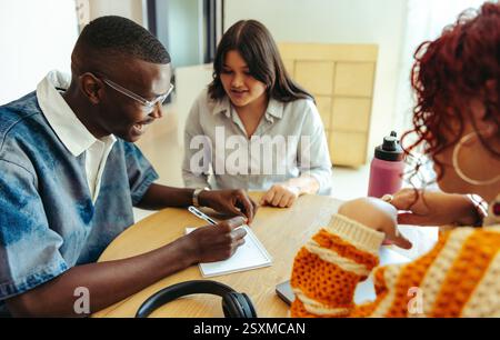 Three friends engage in a study session to prepare for exams, highlighting collaboration and learning in a cozy, naturally lit environment. Stock Photo