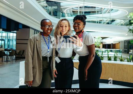 A group of friendly coworkers smiling as they take a selfie together in a modern corporate environment, highlighting teamwork and camaraderie. Stock Photo