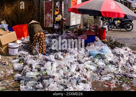 A woman with a conical hat sorts plastic waste in the streets of the historic centre of Hanoi. Stock Photo