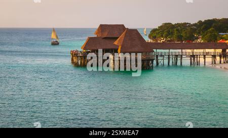 Thatch stilt house restaurant at Kendwa beach at sunset,drone view of turquoise ocean and dhow boat on the ocean,Kendwa beach at Zanzibar,Tanzania. Stock Photo