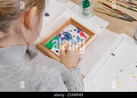 Childs hands coloring in stained glass painting technique picture with wooden frame at masterclass at artisan fair Stock Photo
