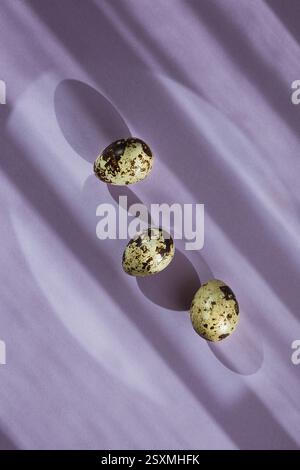 Three quail eggs on pastel purple background, top view, Easter Stock Photo