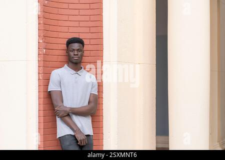 Confident young black man in casual clothes leaning against a red brick wall and white columns Stock Photo
