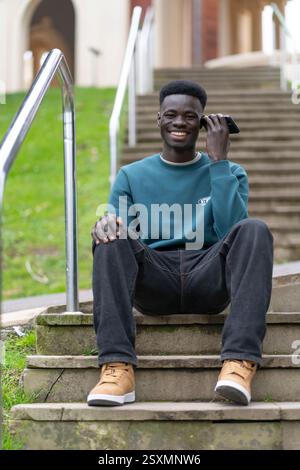 Happy student using his smartphone while sitting on some steps in a university campus Stock Photo