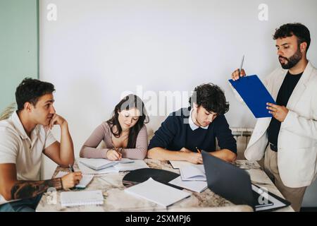High school students engage in a thoughtful discussion with their professor while working on a project. Stock Photo