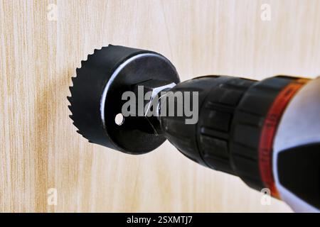 Power drill with sharp hole saw is prepared for creating door lock holes in woodworking projects. Stock Photo