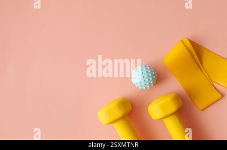Two dumbbells, yoga mat, fitness band and thermos bottle on light pink background, flat lay. Stock Photo