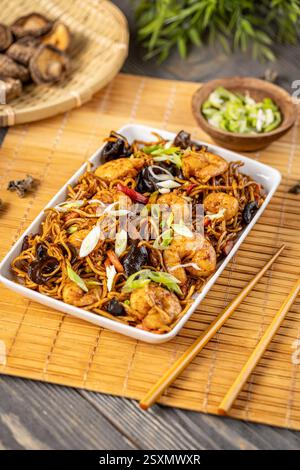 Delicious shrimp and vegetable noodles garnished with chopped green onions, served on a white rectangular plate on a bamboo mat with chopsticks Stock Photo