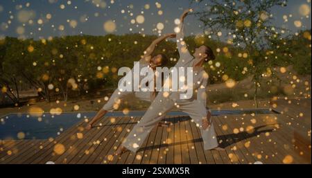 Image of floating light spots over caucasian couple practicing yoga Stock Photo