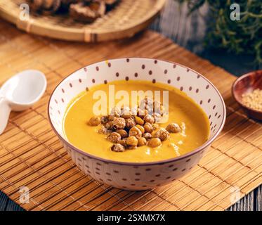 Pumpkin cream soup seasoned with roasted chickpeas, served in a bowl placed on a restaurant table Stock Photo