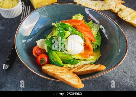 Tasty Caesar salad with eggs, salmon, avocado, cherry tomatoes and grilled toast, close up view. Stock Photo