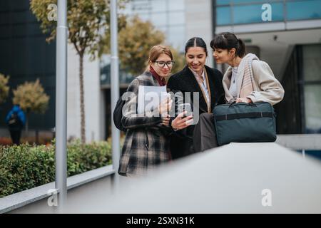 Three professional women collaborating outdoors near an office building Stock Photo