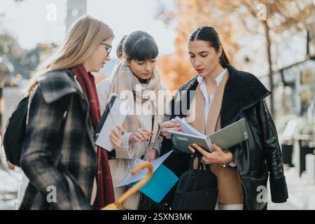 Group of three businesswomen collaborating outdoors during autumn day Stock Photo