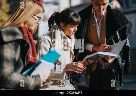 Three multicultural businesswomen collaborating outdoors with documents and notes Stock Photo