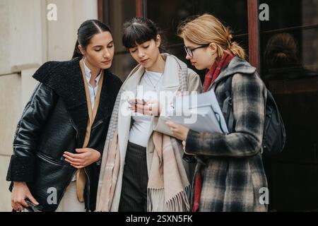 Three professional women collaborating and using smart phone outdoors Stock Photo