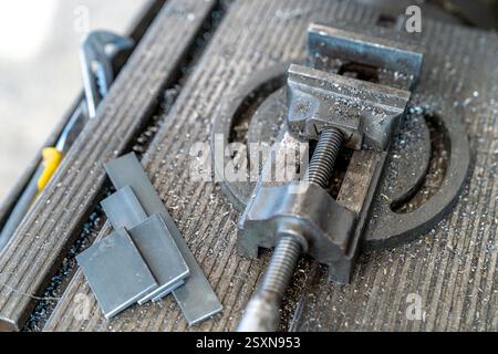 Small bench vise gripping metal pieces on workbench in workshop Stock Photo