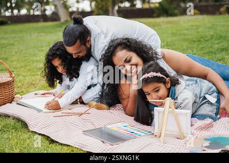 Happy indian family having fun painting with children outdoor at city park - Spring time and parenthood concept - Focus on mother face Stock Photo