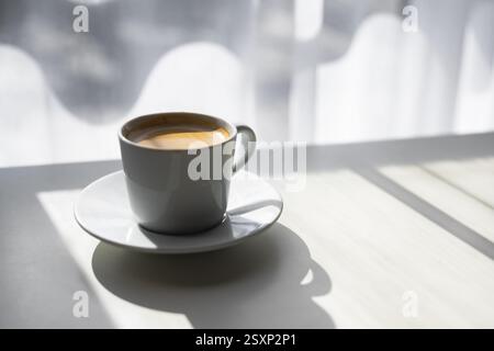 A cup of espresso placed near a sunlit window. Warm morning ambiance in coffee photography Stock Photo