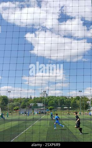Children playing football, on a field of green, synthetic grass on a sunny, gorgeous summer day, with white, delicate and fluffy clouds in the sky Stock Photo