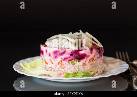 layered vegetable salad with beets and herring, isolated on black background. Stock Photo