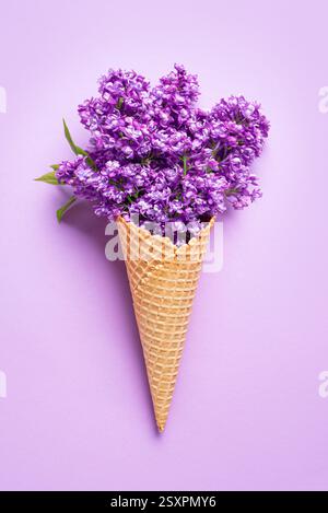 Ice cream waffle cone with purple lilac flowers on pastel background, creative layout, copy space. Spring,  Mothers Day, Valentines Day, bachelorette Stock Photo