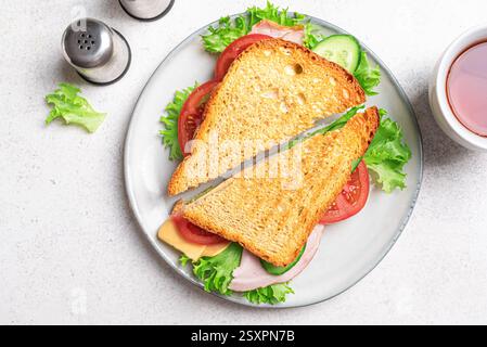 Club sandwich cut in half and cup of tea on white background. Ham and cheddar cheese sandwich with vegetables and lettuce for healthy lunch. Stock Photo