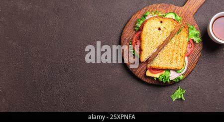 Club sandwich cut in half and tea on dark wooden background, banner, copy space. Ham and cheddar cheese sandwich with tomatoes, cucumber and lettuce f Stock Photo