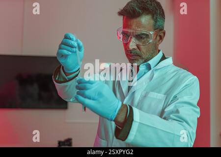 Focused scientist using a pipette for chemical analysis in a high-tech laboratory. Wearing gloves and protective glasses, conducting biotechnology and Stock Photo