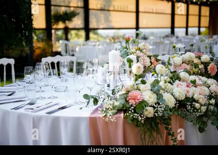 A beautifully arranged table showcases an exquisite floral centerpiece, surrounded by fine glassware and elegant cutlery in a romantic outdoor venue a Stock Photo