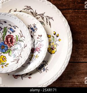 Three antique ornamental plates stacked on a wooden surface. Flowers are painted on the white surface of the plates Stock Photo