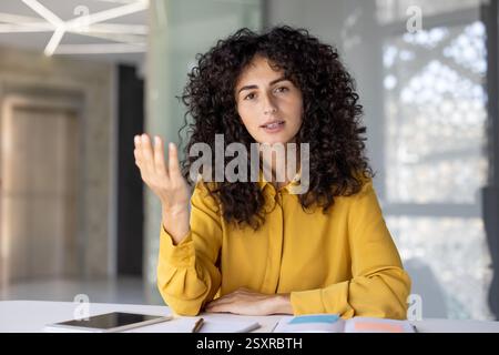 Webcam view, woman serious and focused on online business meeting conference looking at camera. Company employee looking at camera, talking and explaining with colleagues, using video call. Stock Photo