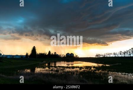 Vibrant sunset over a tranquil farmland pond during a rain shower, creating a dramatic and picturesque scene Stock Photo