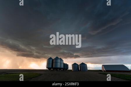 Ominous storm clouds gathering over a farm at sunset, creating a dramatic scene Stock Photo